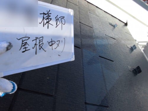 Close-up of a white sign with handwritten Japanese characters resting on dark roof shingles during work.