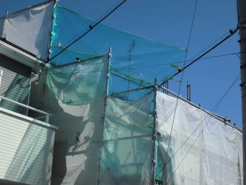 Scaffolding wrapped in green and white construction netting along a building under a clear blue sky