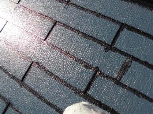 Close-up of blue roof shingles with sunlight reflecting off them; a white sneaker is visible at the bottom edge.