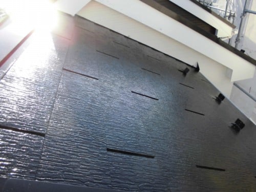 Dark waterproof roof membrane being installed on a sloped roof, with sun glare catching the surface