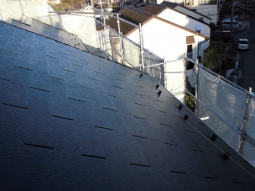 Sloped dark roof with small rectangular vents and scaffolding along the sides of a residential building under construction.
