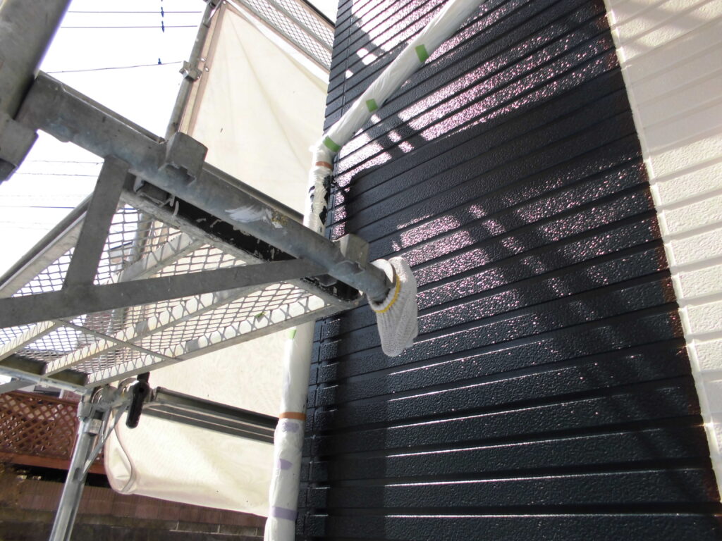 Scaffolding against a dark blue corrugated exterior wall with painted equipment and wrapped pipes nearby.