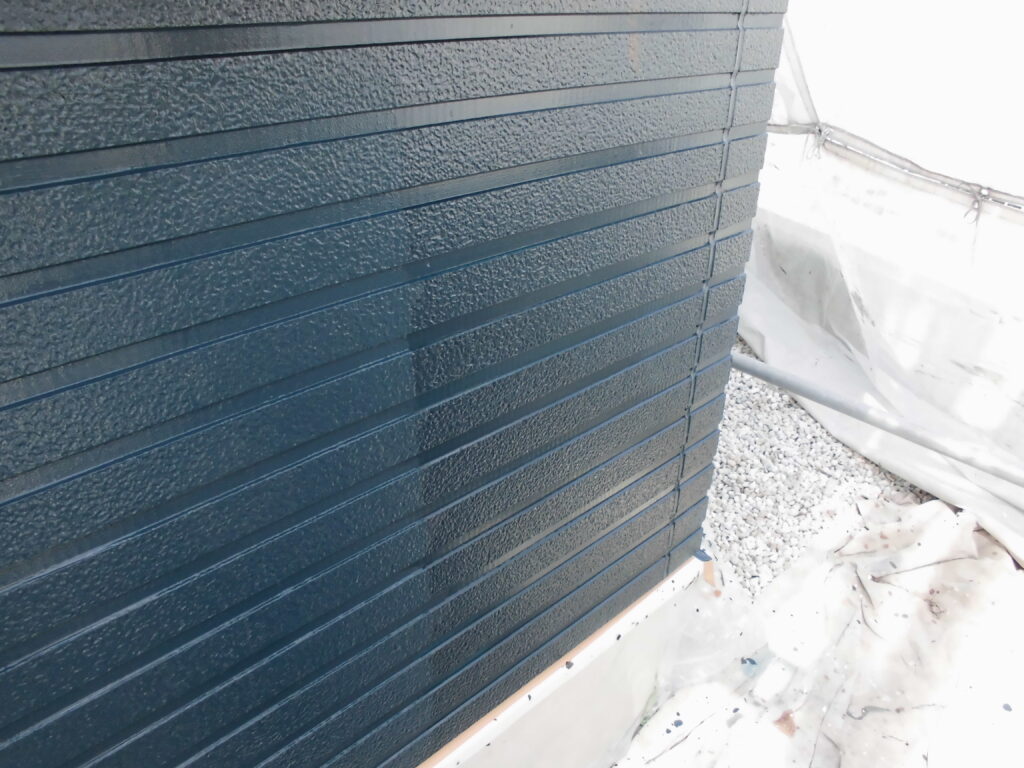 Blue corrugated metal exterior wall panels with a white tarp and gravel at the base (construction site).