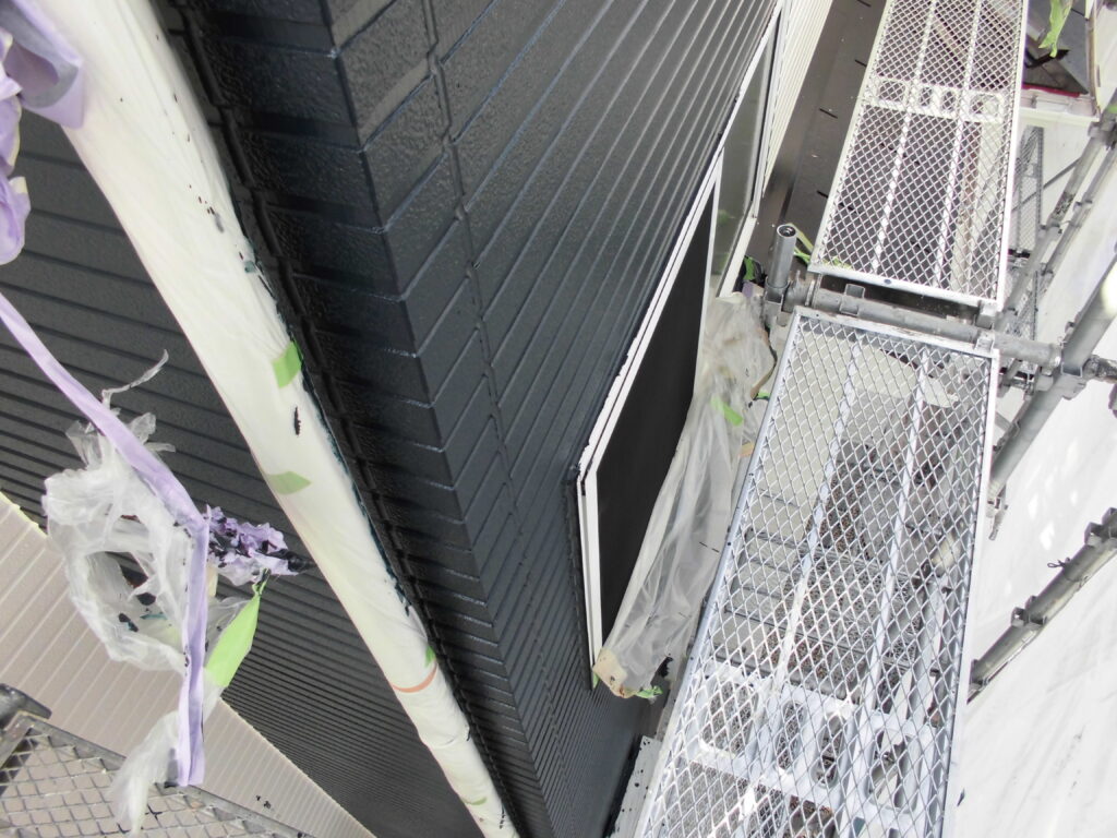 Exterior construction scaffold along a dark wall, with metal mesh platforms and protective plastic wrapping nearby.