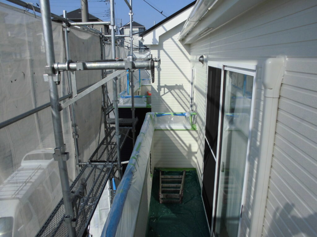 Narrow exterior balcony under construction with metal scaffolding on the left and a sliding glass door on the right.