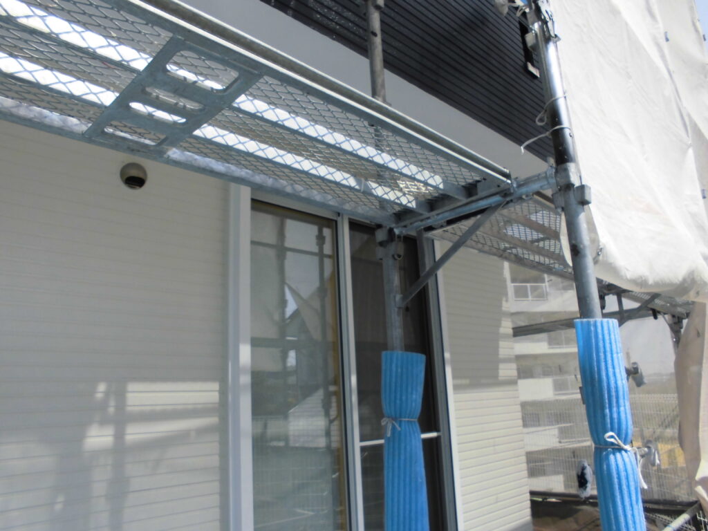 Construction scaffold attached to a house with blue protective padding on poles and a sliding glass door beneath new siding.