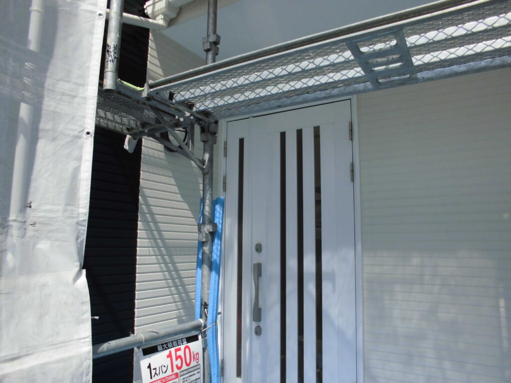 White exterior door with vertical glass panels under metal scaffolding; a 150 kg load sign is visible on the scaffolding.