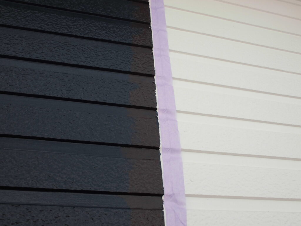 Two-tone exterior wall with dark left siding and light right siding separated by purple painter's tape along the seam.