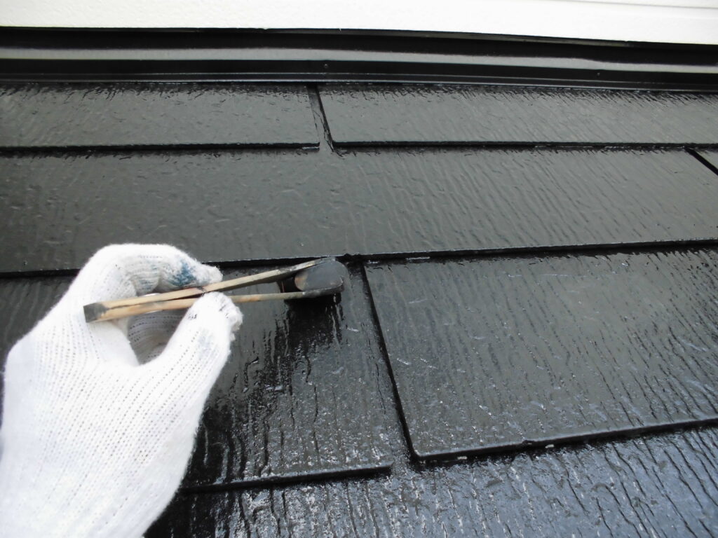 Gloved hand using a small tool to lift a black roof shingle during maintenance.