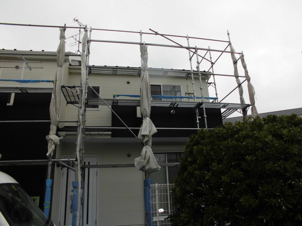 Two-story house under construction surrounded by metal scaffolding and white protective wrap.