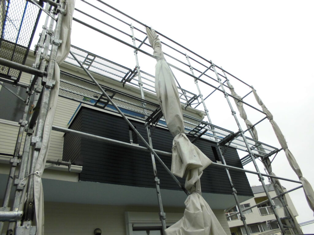 Scaffolding surrounds a modern two-story house with white protective tarps tied to metal poles under construction.
