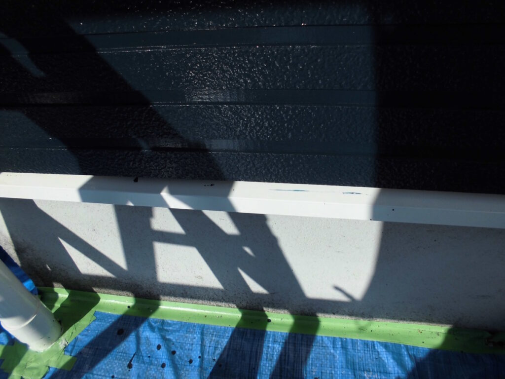 Shadow of scaffolding on an exterior wall, with a blue tarp and green painter’s tape on the ground beneath
