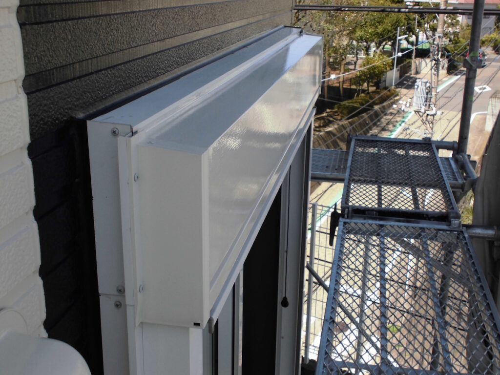 White rectangular utility box mounted on the side of a building with metal scaffolding and a street below.
