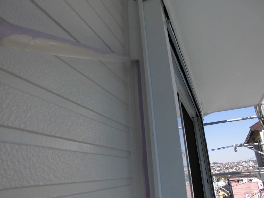 Corner of a balcony with white horizontal siding, a sliding door, and painter's tape along the frame; city rooftops visible beyond.