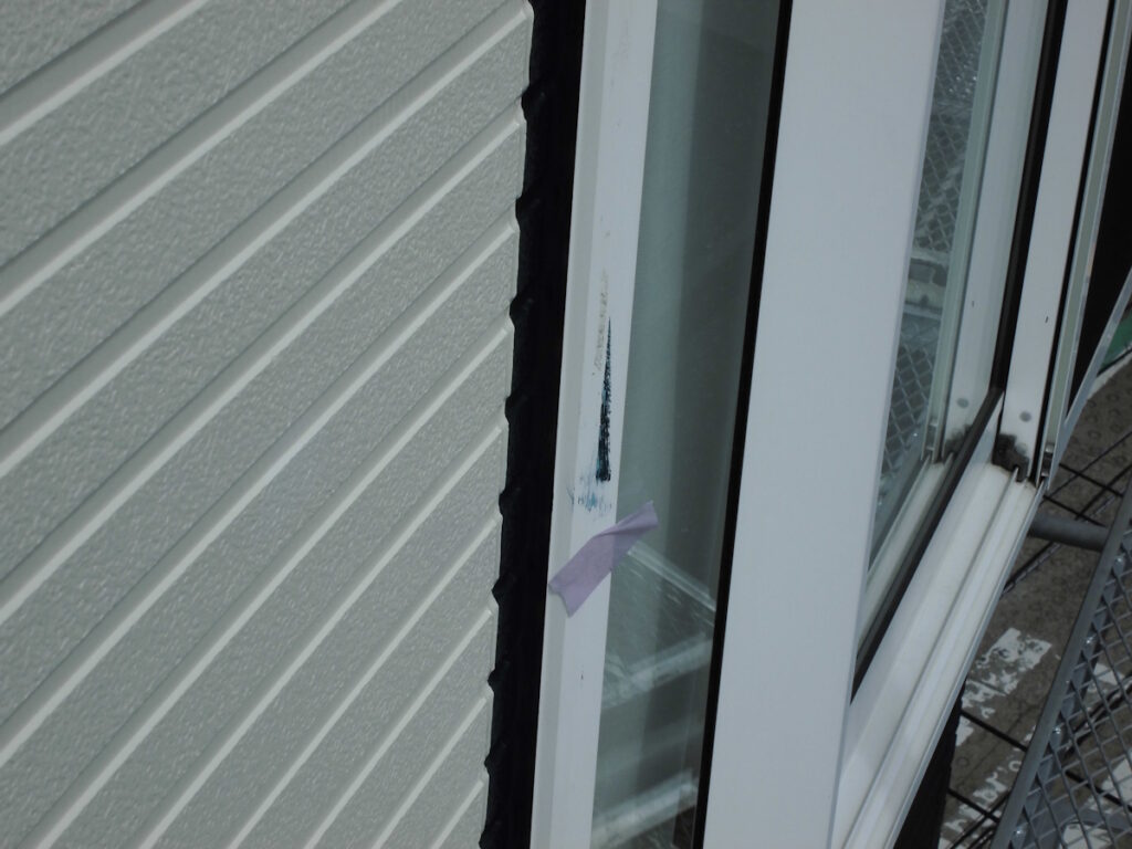 Close-up of a white window frame with a damaged black seal along the edge and a small piece of purple tape attached.