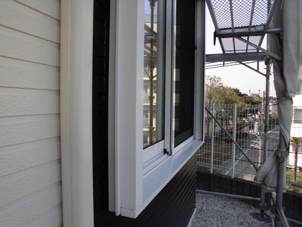 Open white-framed window on a light-colored house with construction scaffolding outside and gravel ground nearby.