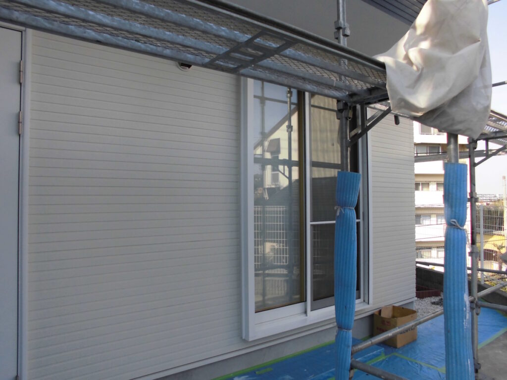 Construction scaffolding along a house with blue protective wraps around posts and a sliding window nearby.