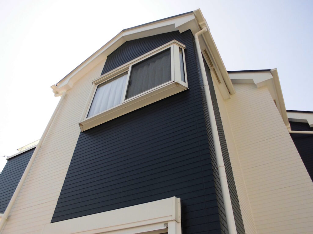 Angle view of a modern house with dark blue siding and white trim, showing a bay window.