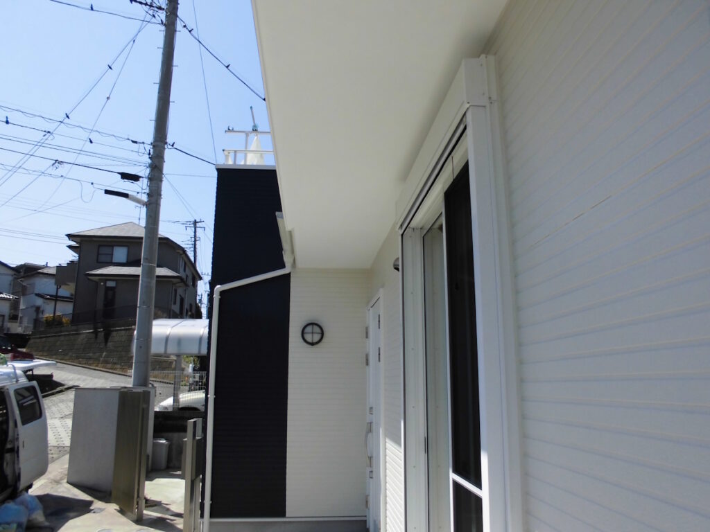 White siding house exterior with a sliding glass door and a black vertical accent wall under a bright blue sky