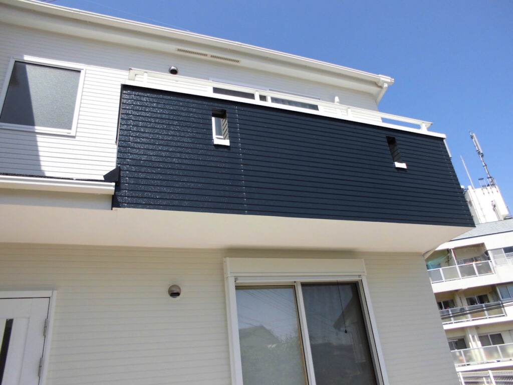 White two-story house with a dark navy balcony wall and large sliding glass door, under a clear blue sky.