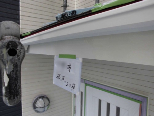 Handwritten sign in Japanese taped to the exterior of a light-colored house under the eaves.