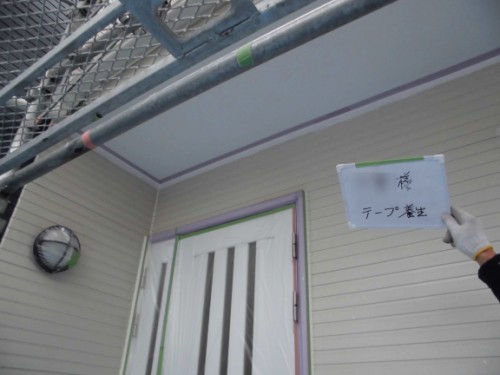 Gloved hand holding a sign with Japanese text near a house under construction, with scaffolding overhead and taped edges around the doorway.