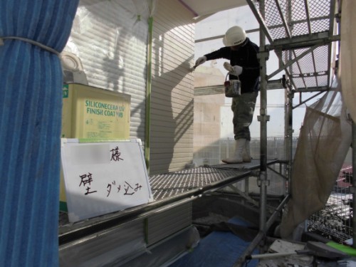 Construction worker in a hard hat and white boots applying finish coat to an exterior wall from scaffolding.