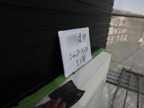 Close-up of a hand sanding a white surface on a balcony ledge, with a small whiteboard sign resting against a black wall.