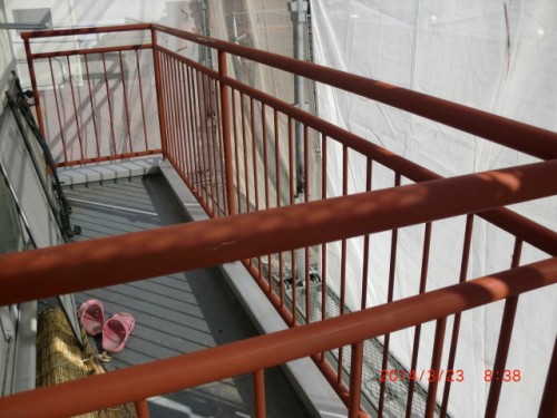 CIMG0382 | 外壁塗装は神奈川県横浜市の塗装職人 Red metal guardrails along a construction balcony; pink slippers on the gray decking with scaffold and tarps in the background.