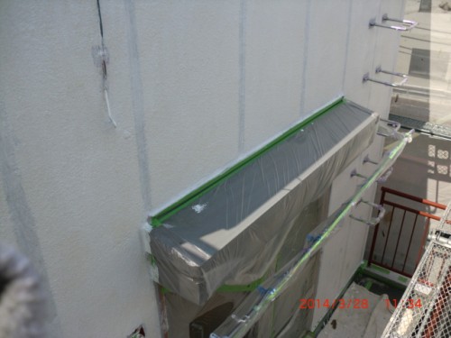 CIMG0396 | 外壁塗装は神奈川県横浜市の塗装職人 Exterior building wall with a balcony covered in plastic sheeting secured with green tape; scaffolding on the right, indicating ongoing construction or protection work.