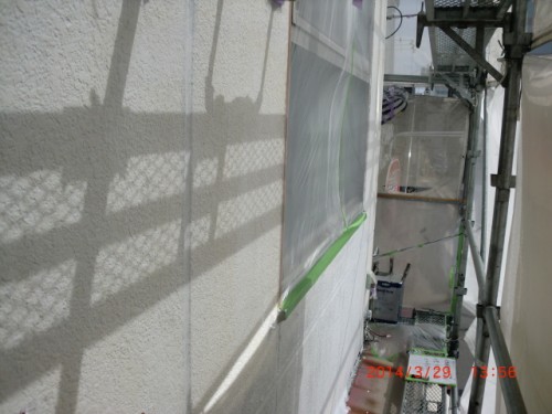 CIMG0407 | 外壁塗装は神奈川県横浜市の塗装職人 Exterior wall under construction with scaffolding and protective plastic; a green level rests against the wall, shadows of the scaffold visible on the surface.