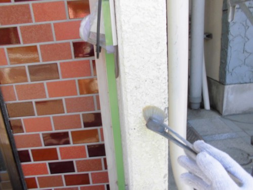 CIMG1383 | 外壁塗装は神奈川県横浜市の塗装職人 Person wearing a white-gloved hand brushes a white stucco column beside a brick wall during painting.