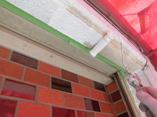 CIMG1385 | 外壁塗装は神奈川県横浜市の塗装職人 Close-up of a paint roller applying white paint to a door frame, with green masking tape and red brick wall nearby.