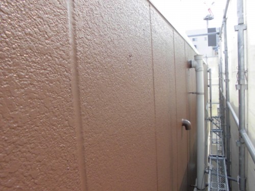 CIMG1391 | 外壁塗装は神奈川県横浜市の塗装職人 Brown textured exterior wall with pipes protruding in a narrow alley lined with scaffolding on the right.