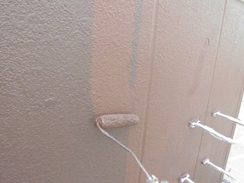 CIMG1393 | 外壁塗装は神奈川県横浜市の塗装職人 Close-up of a paint roller applying brown paint to a textured exterior wall (stucco).