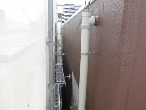 CIMG1395 | 外壁塗装は神奈川県横浜市の塗装職人 Narrow alley between two buildings with scaffolding on the left and a white vertical pipe attached to the brown wall on the right.