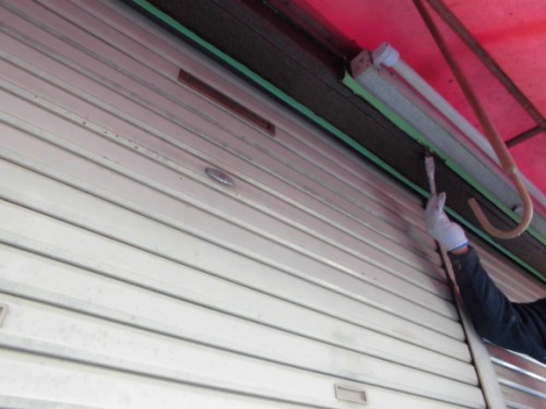 CIMG1396 | 外壁塗装は神奈川県横浜市の塗装職人 Person wearing gloves using a paint roller to apply white paint to a metal rolling shutter.