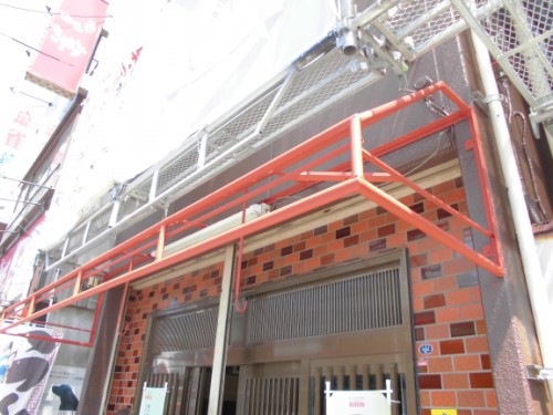 CIMG1424 | 外壁塗装は神奈川県横浜市の塗装職人 Orange scaffolding runs along the front of a brick storefront over the entrance.