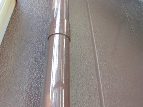 CIMG1434 | 外壁塗装は神奈川県横浜市の塗装職人 Close-up of a glossy brown metal pipe with a clamp ring against a textured brown surface.