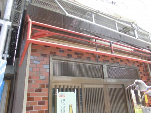 CIMG1441 | 外壁塗装は神奈川県横浜市の塗装職人 Brick storefront under construction with scaffolding and red pipes above a metal door; Kirin sign visible.