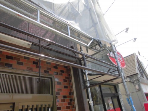 CIMG1442 | 外壁塗装は神奈川県横浜市の塗装職人 Scaffolding and plastic sheeting cover the exterior of a brick storefront under renovation.