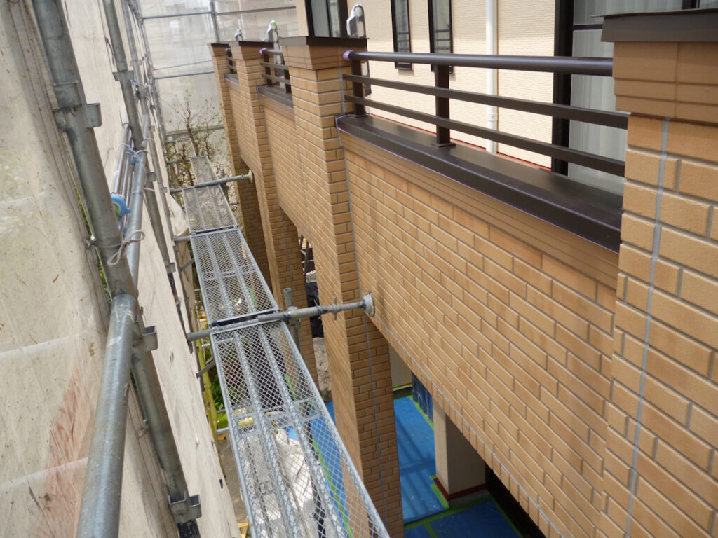 Construction scaffold runs along a brick building with metal safety rails and a narrow metal walkway between walls.