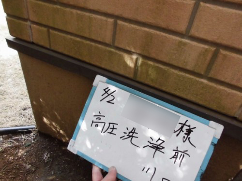 Person holding a whiteboard-style sign with handwritten Japanese text in front of a brick exterior wall, outdoors.