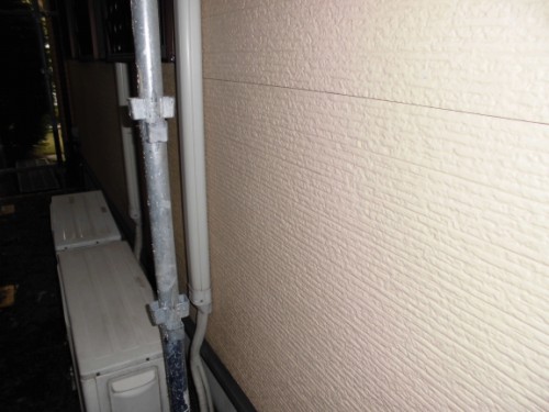 Side view of a beige textured exterior wall with scaffolding pipe and an outdoor air conditioner unit nearby.