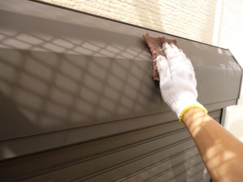 Gloved hand wiping a brown metal rolling shutter with a cloth outside the building