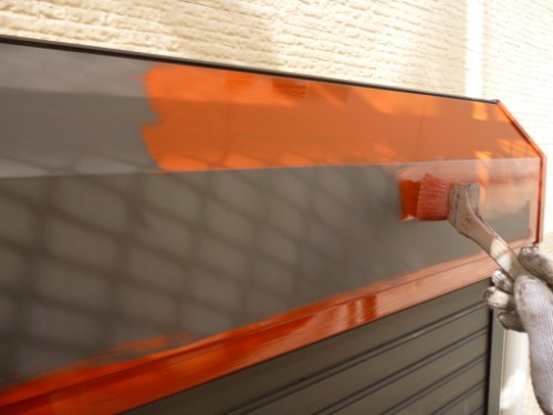 Person paints an orange stripe on a metal rolling shutter with a brush close-up. (Informative)