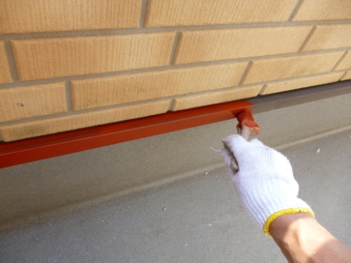Close-up of gloved hand applying red caulk along the base of a brick wall.