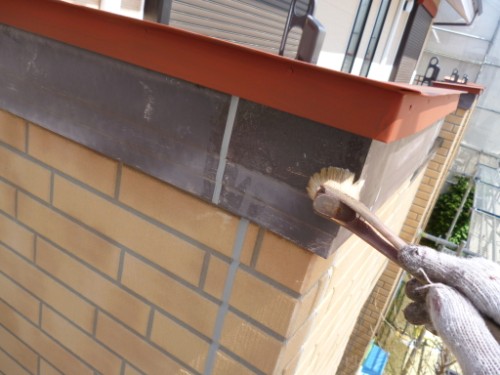 Close-up of a gloved hand painting the top edge of a brick wall with a small brush on an orange coping cap.