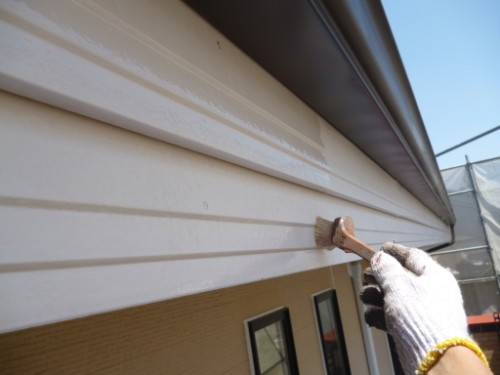 Person painting exterior white siding with a small brush, wearing gloves.