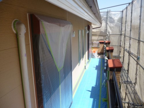 Exterior of a house under renovation with plastic-covered windows and taped seams, blue protective flooring along the walkway, and scaffolding nearby.